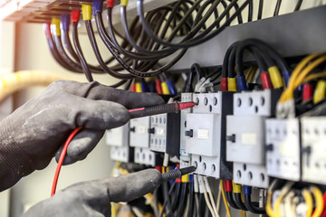 Electrical engineer using measuring equipment to checking electric current voltage at circuit breaker and cable wiring system for maintenance in main power distribution board.
