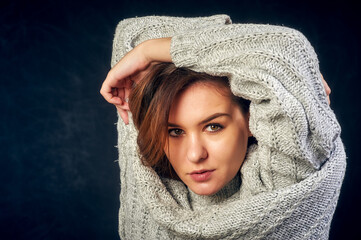 Obraz premium Portrait of a young beautiful girl in a warm knitted sweater on a dark background