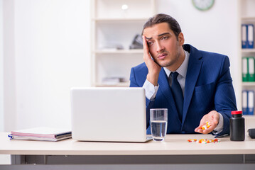 Young male employee and a lot of pills on the desk