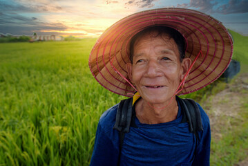 Asian farmer An Asian senior or an elderly man wearing a hat stands smiling happily at a rice field in Vietnam.