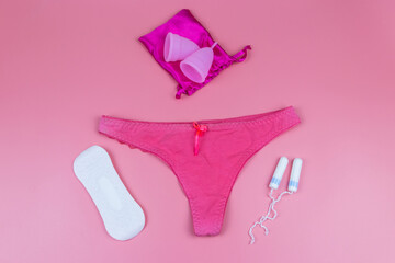 Women's panties with menstrual cups, sanitary pads and tampons on pastel pink background. Top view. Concept of critical days, menstruation, feminine hygiene