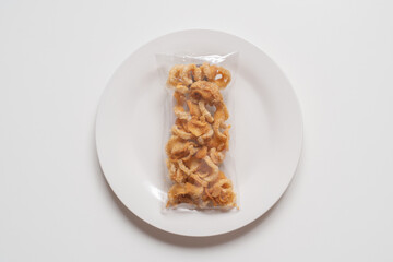 pork snack, pork rind, pork scratching without fat caps in plastic bag on white plate and white background