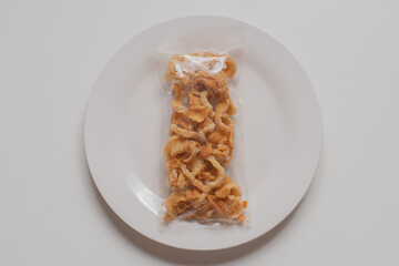 pork snack, pork rind, pork scratching without fat caps in plastic bag on white plate and white background