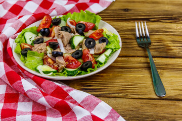 Tasty tuna salad with lettuce, black olives and fresh vegetables on wooden table