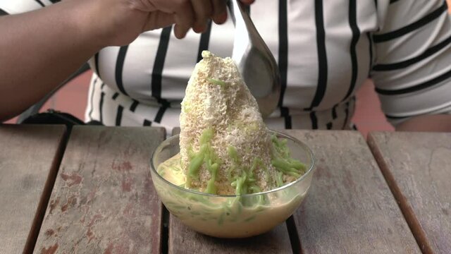 Close up view of woman using spoon to eat famous dessert cendol in fine shaved ice at a restaurant