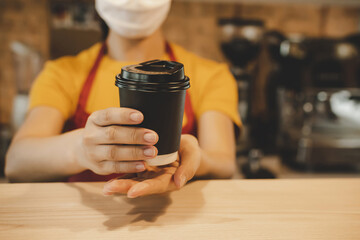 Fototapeta na wymiar friendly woman barista or waitress wearing protection face mask waiting for serving hot coffee cup to customer in cafe coffee shop, cafe restaurant, service mind, new normal, food and drink concept