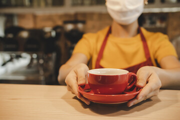 friendly waitress woman wearing protection face mask waiting for serving hot coffee cup to customer in cafe coffee shop, cafe restaurant, service mind, new normal, food and drink delivery concept