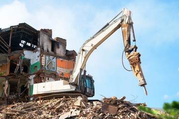 An excavator demolishes a brick house. Renovation concept of old dilapidated housing.