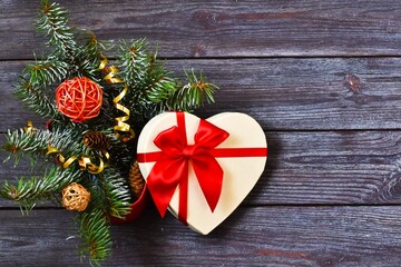 Gift box heart with beautiful red ribbon with fir branch on wooden background. Concept for christmas, new year, greeting card. Copy space, top view.