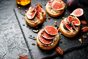 Sandwiches with ricotta cheese, fresh figs, pecan nuts and honey on black stone background