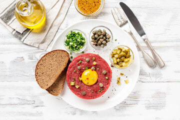 Beef tartare with capers , fresh onion and pickled cucumber on white plate on white wooden background.	