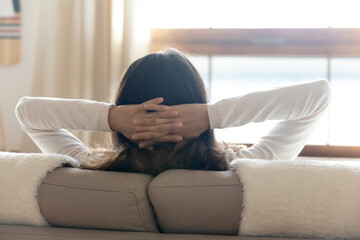 Amazing siesta. Back shot of carefree young woman sitting on soft couch with hands behind head...