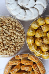 Four jars of Nastar (Dutch pineapple tarts), Kaasstengels (Dutch cheese finger cookies), Vanillekipferl (Austrian crescent shaped vanilla biscuits), and Fried Peanuts on a table. Half composition.