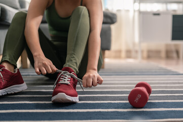 Naklejka premium A woman is wearing shoes to exercise in her home. Exercise indoors during quarantine. Exercise, Workout at home activities.