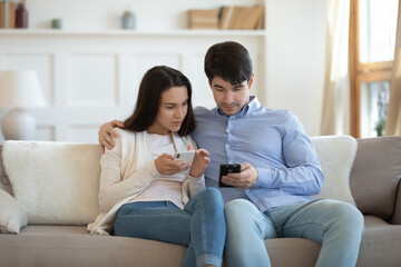 Obraz premium I drop you photo, catch it! Young man and woman in love relaxing on sofa together using gadgets, sharing interesting information by wifi connection, sending one another pictures, music or video files