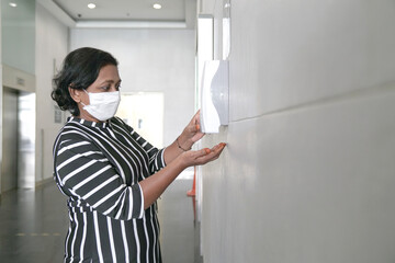 Businesswoman wearing face mask using sanitizer liquid from dispenser