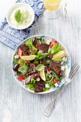 Tasty Salad with Grilled Beef Pieces, Cherry Tomatoes, feta Cheese and Kalamata Olives. Bright wooden background. Top view.