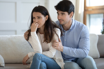 Can we try to make peace. Young boyfriend husband embracing shoulders of crying nervous offended girlfriend wife proposing to make peace, reconcile after quarrel, supporting comforting at hard time