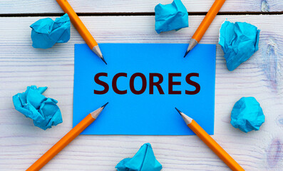 SCORES - word on blue paper on a light background with crumpled pieces of paper and pencils