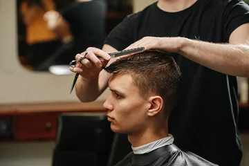 Fotobehang Indifferent loof young man in a barber shop getting a trim, close up. © zzzdim