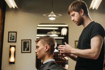 Keen hairdresser making a haircut for a young man in a barber shop