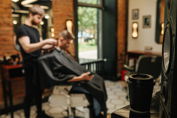 Blurred image of male hairdresser making haircut and coffee in foreground