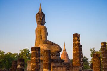 Ancient sculpture of a seated Buddha on the ruins of a Buddhist temple in the evening light. Sukhothai, Thailand