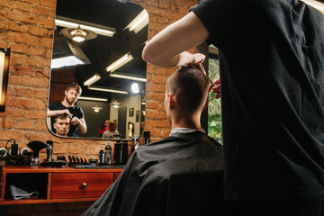 Image of hairdresser making a haircut for a young man in a barber shop