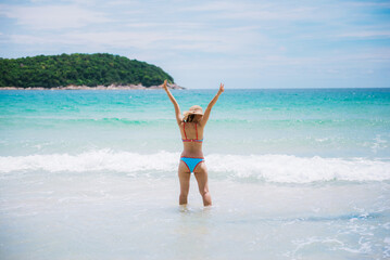 Rear view of the young asian woman in hat relaxing on the beach and looking at the sea. Travelling tour in Asia : Phuket, Thailand.