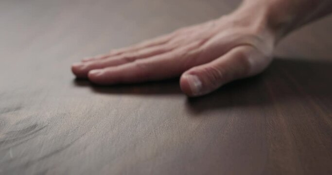 Slow motion of man hand checking toned walnut table surface with oil finish