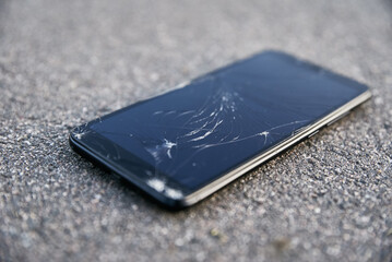 Damaged smartphone with broken touch screen on asphalt