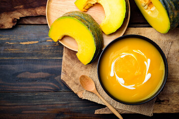 Pumpkin soup in a bowl with spoon and fresh pumpkins on wooden table, Top view