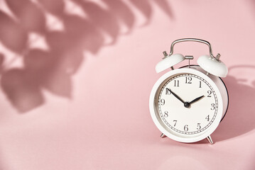 White alarm clock and leaves shadows on pastel pink background