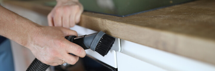 Close-up of man from professional cleaning service clean kitchen furniture with vacuum cleaner. Handyman prepare room after renovation. Cleanliness and household concept