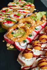 A set of baked sushi rolls lies on bamboo leaves served on black stone slate. Dark background