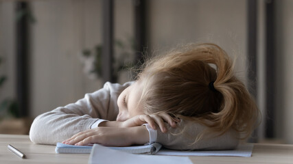 Close up tired little girl sleeping at work desk, lying on notebooks, exhausted child schoolgirl...