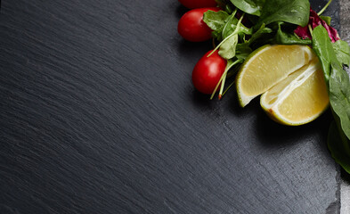 Lime, lettuce, greens and red cherry tomatoes lie on a dark stone slate background, space for text, restaurant menu