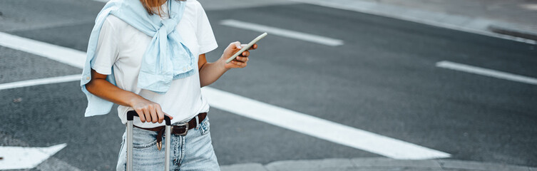 Young traveling woman with suitcase on a sunny city street. Traveler on vacation. Waiting for taxi