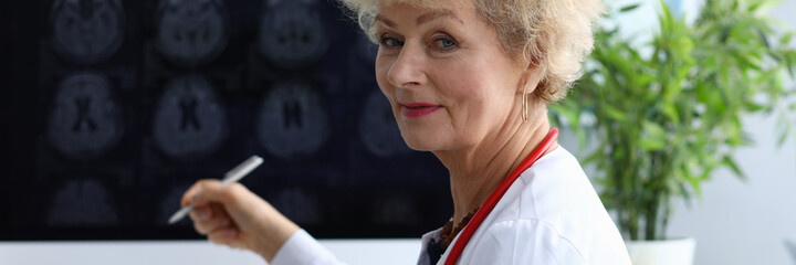 Portrait of professional senior female doctor holding silver pen with prescription. Medical worker wearing uniform and red stethoscope. Modern medicine and qualified specialist concept