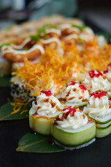 A set of baked sushi rolls lies on bamboo leaves served on black stone slate. Dark background