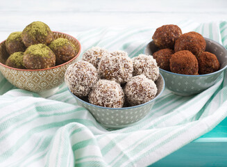 Home made vegan energy protein balls - coconut, matcha and chocolate cocoa made with nut butter, oats and seeds served in bowls on turquoise napkin. Closeup