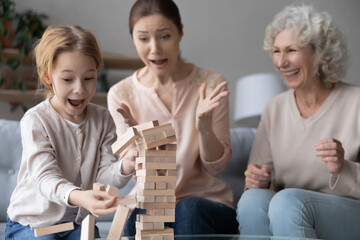Laughing little girl with mother and grandmother playing crash and stack board game, catching...