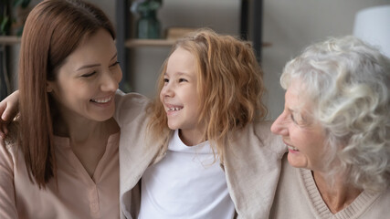 Close up pretty little girl having fun with young mother and mature grandmother, hugging, cuddling, enjoying tender moment, three generations of women enjoying leisure time together at home