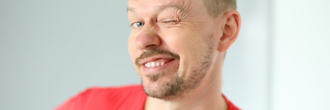 Portrait Of Funny Cute Man Posing On Camera. Joyful Person Making Faces. Mature Middle-aged Male In Red Tshirt. Adult Winking Standing Indoors. Modern Concept