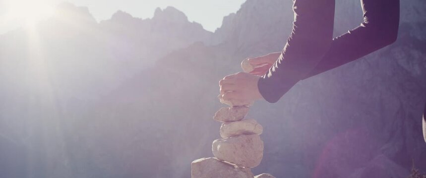 Woman put stone with hand on cairn zen meditation mindfulness on an autumn hiking travel in protected mountain nature in the Alps close up slow motion flare beautiful light