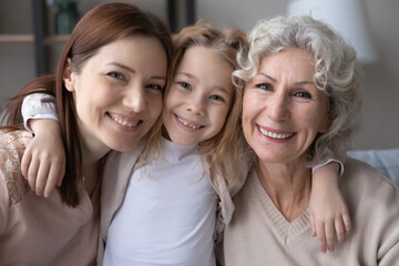 Head shot portrait smiling pretty little girl hugging young mother and mature grandmother, three...
