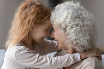 Close up smiling mature grandmother and little granddaughter touching foreheads, enjoying tender moment together, happy overjoyed elderly grandma and preschool girl hugging, love and care