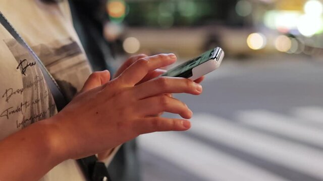 夜の渋谷でスマホを操作する若い女性の手元