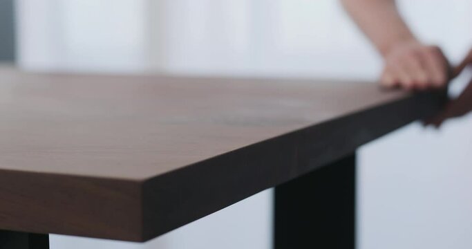 Slow motion of man hand sanding toned walnut table surface before applying finish