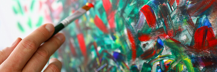 Close-up of persons hand creating abstract painting on canvas holding paintbrush. Picture with mixed colours. Creative and talented young artist. Masterpiece and modern art concept